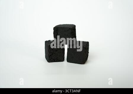 Black shisha charcoal cubes stacked on clean white background, symbol of smoking, relaxation, fire, and lifestyle concepts.  Stock Photo