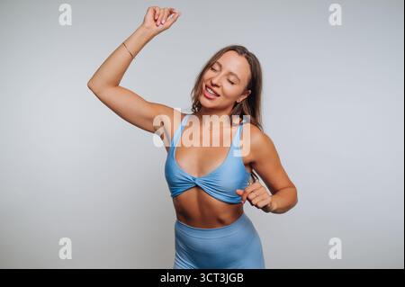 A joyful young woman is dancing gracefully while wearing a light blue outfit. She has a big smile and appears to be enjoying the music in a bright stu Stock Photo