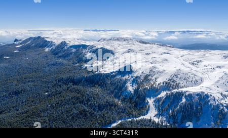 Majestic aerial view of Jahorina mountain covered in fresh snow under bright blue sky, showcasing forested slopes and panoramic alpine scenery Stock Photo