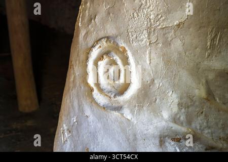 Close-up of prehistoric ancient spiral symbol carved in whitewashed wall of reconstructed Neolithic-style dwelling Irish heritage roundhouse, Wexford. Stock Photo