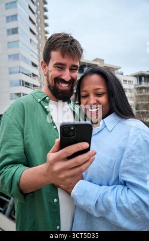 Happy multiracial couple using smartphone outdoors in the city Stock Photo