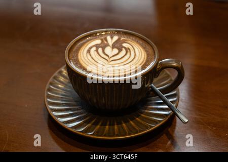 Cuppa of aromatic hot cafe mocha with lovely heart shaped art served in brown cup and saucer on brown table top Stock Photo