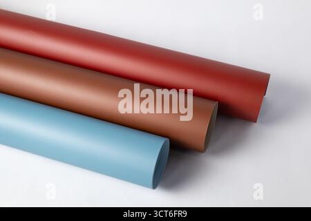 Seamless background rolls in matte red, earthy brown, and pale blue, diagonally stacked on a clean white surface for studio photography, crafting, or Stock Photo