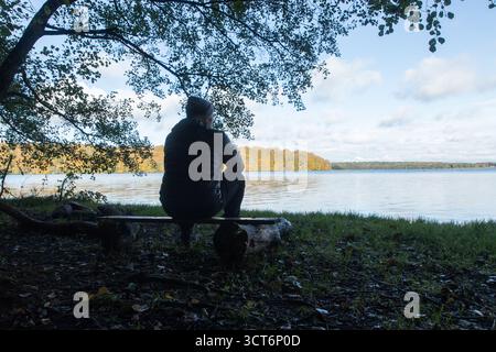 man sitting anole on bench at lake looking and thinking about life Stock Photo