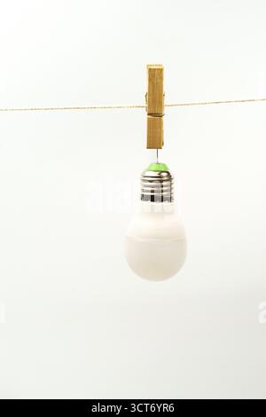 Light bulb hanging from a clothespin on a string against a white background Stock Photo