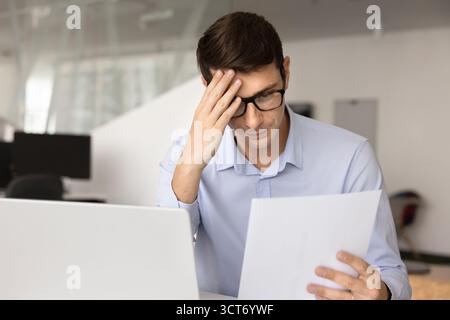 Confused accountant man in glasses touching head and reading document Stock Photo