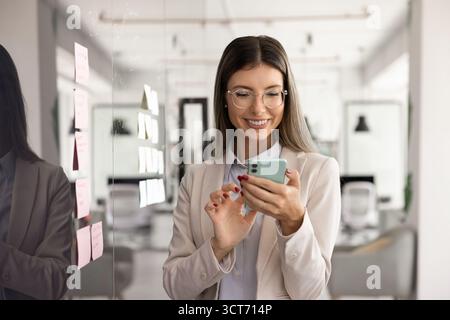 Happy young business leader woman typing on smartphone Stock Photo