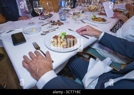 Steak with vegetables and pasta in an elegant table setting with white wine glasses and cloth napkins Stock Photo