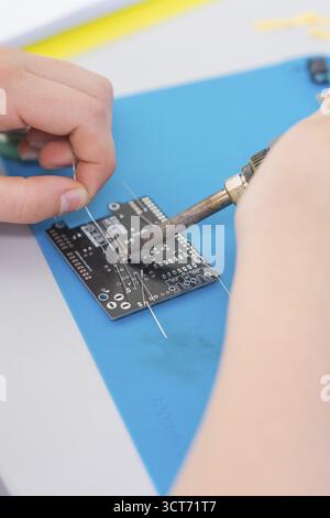 Person soldering an electronic circuit board with a soldering iron on a blue mat Stock Photo