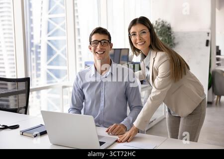 Happy young business professionals sitting and standing at laptop Stock Photo