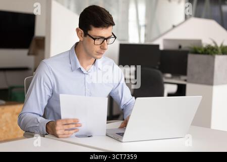 Focused young Latin professional man in glasses using accounting application Stock Photo