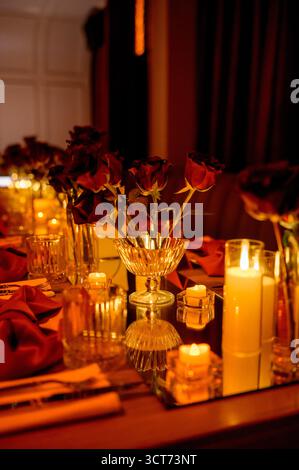 Close-up of a long table with flowers and burning candles in a dark room. a set table with red decor and lights Stock Photo