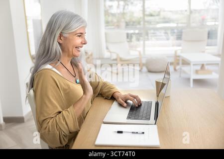 Happy senior Hispanic woman typing on laptop, using computer Stock Photo
