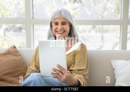 Happy senior grey haired woman using tablet pc Stock Photo