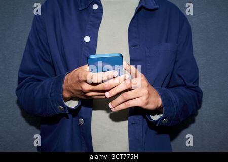 Young Man Using Smartphone While Standing Against Wall Stock Photo