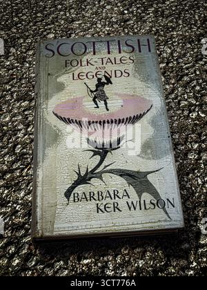 Minimalist still life image of an old hard backed book entitled Scottish Folk Tales and Legends by Barbara Ker Wilson placed on an asphalt roadway Stock Photo