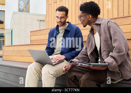 Young Multiethnic Men Collaborating Outdoors Using Laptop and Tablet Stock Photo