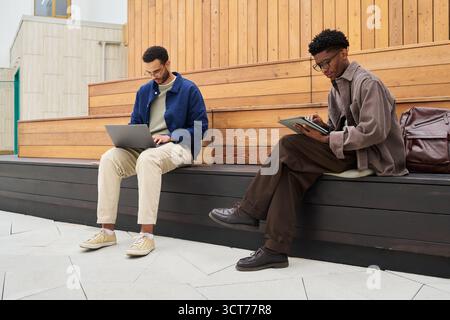 Young Man and Black Man Working Remotely Using Laptop and Tablet Stock Photo