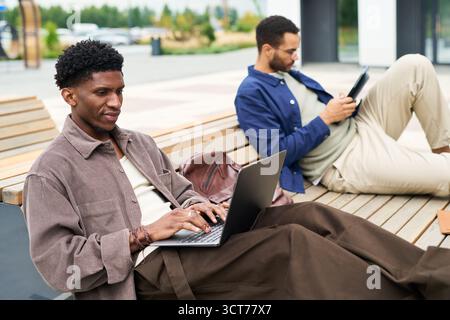 Two Young Men Using Devices Outdoors Stock Photo
