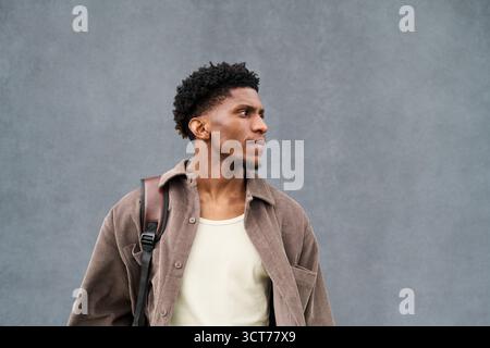 Young Black Man Standing Outdoors Looking Away with Backpack Stock Photo