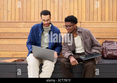 Young Men Collaborating on Laptop and Tablet in Modern Outdoor Setting Stock Photo