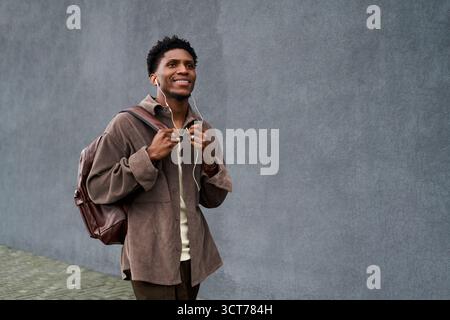 Young Black Man Walking Outdoors Listening to Music with Backpack Stock Photo