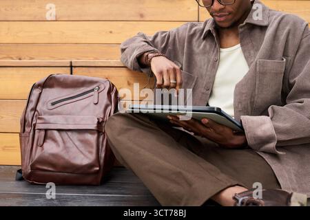 Young Black Man Sitting Outdoors Using Digital Tablet for Studying Stock Photo