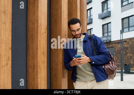 Young Black Man Standing Outdoors Using Smartphone near Modern Building Stock Photo