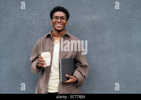 Portrait of Young Black Man Smiling While Holding Coffee and Notebook Stock Photo