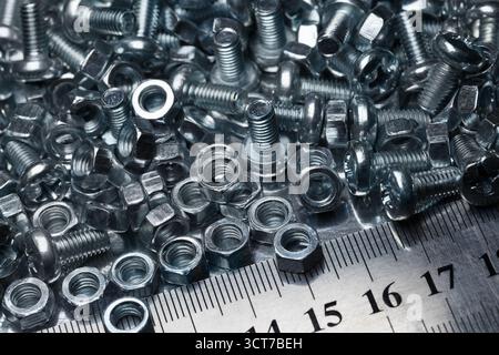 Lots of small screws and nuts scattered in a heap and a metal ruler Stock Photo