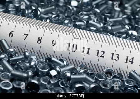 Lots of small screws and nuts scattered in a heap and a metal ruler Stock Photo