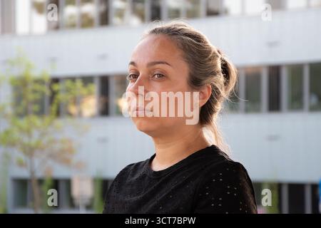 A 40-45 year old woman in black clothes stands on the street in front of a modern building with a serious expression Stock Photo