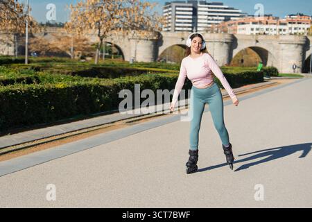 Young woman rollerblading outdoors, smiling while exercising and listening to music Stock Photo