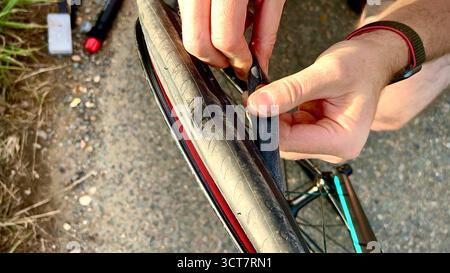A close-up photograph of a man fixing a bicycle puncture, showing only his hands and part of the tyre. Stock Photo