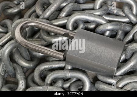 Silver colored padlock unlocked on pile of chains industrial still life security concept. Stock Photo