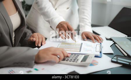 Two professional businesswomen are collaborating and analyzing financial reports, charts, and market data on a desk, using calculator to check figures Stock Photo