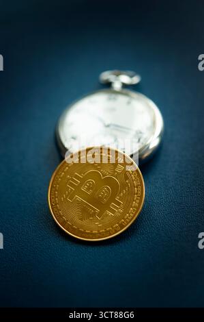Bitcoin coin with pocket watch on blue surface representing time and value in cryptocurrency investment and financial growth Stock Photo