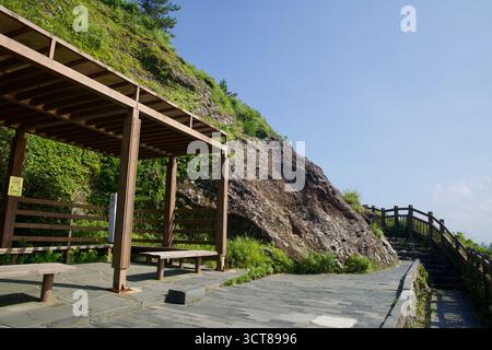 A wooden rest shelter with benches sits beside the paved trail on Seongsan Ilchulbong, a no‑smoking notice on its post, while the path curves around a Stock Photo