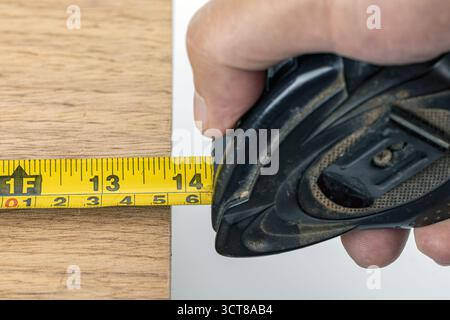 A hand holding measuring tape wood carpenter measure closeup tool yellow inch workshop. precise measurement oak board steady grip practical and focuse Stock Photo