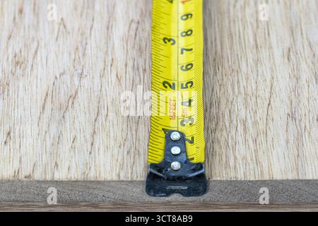 A measuring tape yellow metal wood closeup tool metric imperial inch scale snug focus measuring tape against wood board, precise craft mood, workshop Stock Photo
