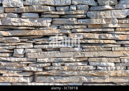 A close-up view of a stacked gray stone wall built from irregularly shaped rocks. Natural texture and rugged craft convey rustic charm, durability, an Stock Photo