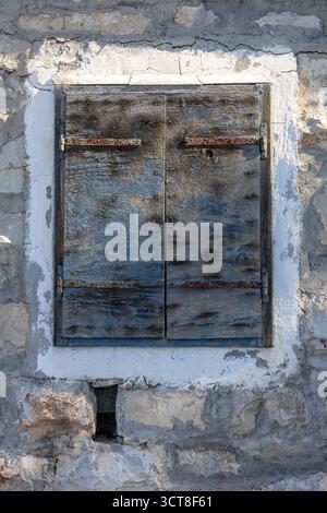 A weathered pair of wooden shutters covers an old stone wall, featuring rusted hinges and chipped paint. The aged texture evokes rural charm, history, Stock Photo