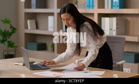 Busy focused Asian Chinese business woman joyful female CEO employer Korean Japanese businesswoman worker analyzing documents report paper searching Stock Photo