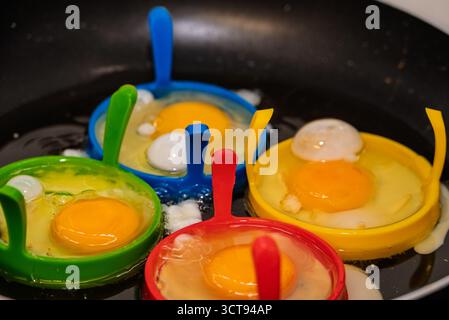 Eggs are being cooked in colorful silicone molds in a frying pan, for a fun and easy breakfast. Stock Photo