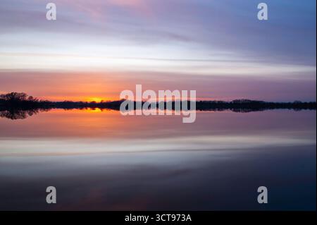 Tranquil Sunset Over Calm Lake With Silhouetted Trees And Vibrant Reflections At Dusk Stock Photo