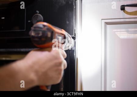 A man installs an oven into a cabinet using a drill, demonstrating the process of installing appliances. Stock Photo