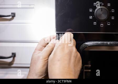 A man carefully adjusts the installation of a modern kitchen oven while installing it in a cabinet. Stock Photo