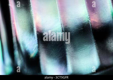 Abstract close-up of textured glass surface with smooth ridges, reflecting soft hues of green, blue, purple, and pink light, creating an iridescent, m Stock Photo