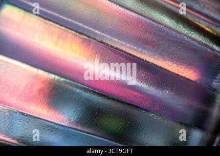 Abstract close-up of textured glass surface with metallic sheen, reflecting vibrant streaks of green, red, orange, and yellow light, creating a colorf Stock Photo