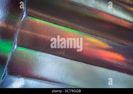 Abstract close-up of textured glass surface with metallic sheen, reflecting vibrant streaks of green, red, orange, and yellow light, creating a colorf Stock Photo